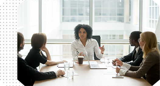 woman in white dress shirt sitting at head of conference table talking to colleagues